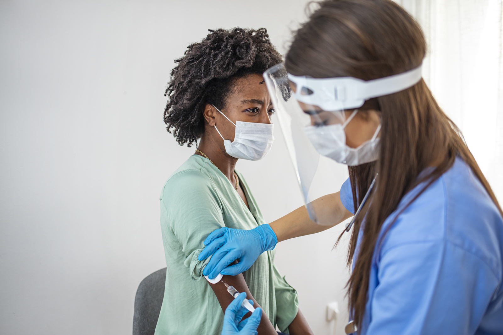 女护士戴防护面罩和手套准备医用注射器为患者注射的侧视镜头。冠状病毒免疫