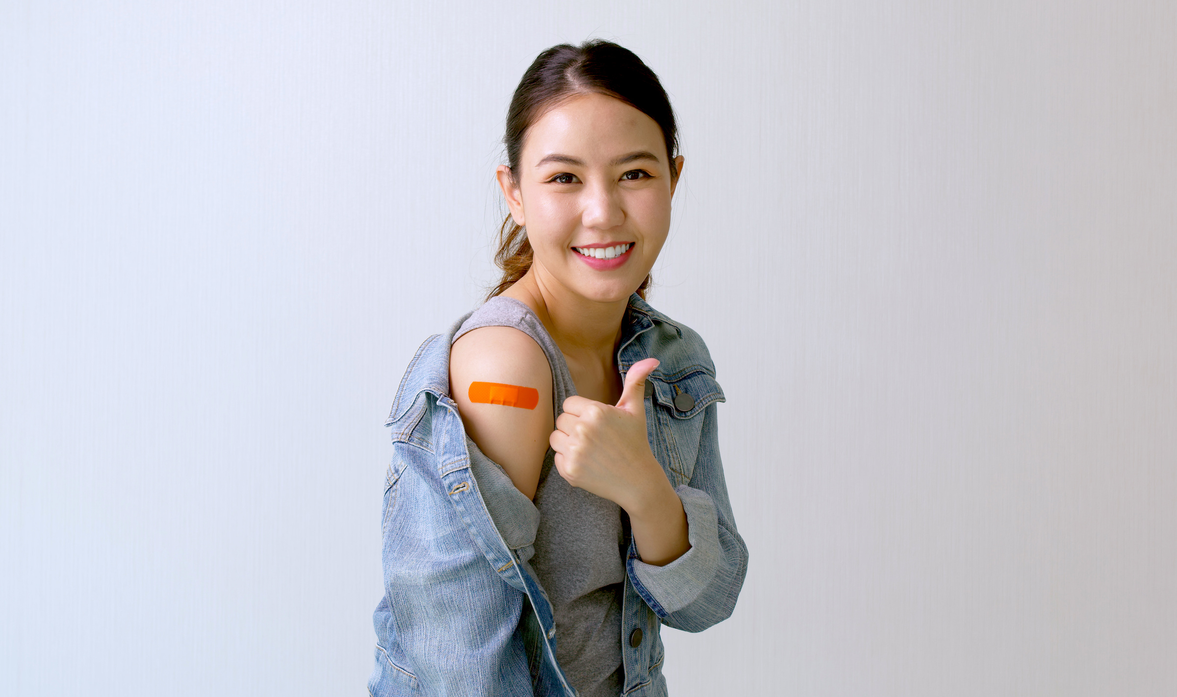 Young attractive female or teenage receive covid-19 anti virus vaccine in campaign vaccination safe life happy smile cheerful with blue, yellow, pink bandage on arm with copy space.