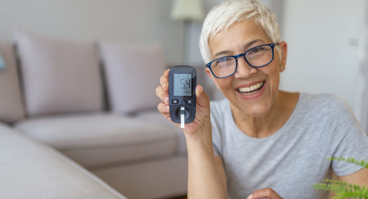 Older lady smiling as she tests her blood sugar levels