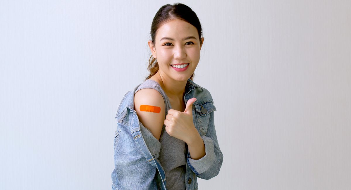 Young attractive female or teenage receive covid-19 anti virus vaccine in campaign vaccination safe life happy smile cheerful with blue, yellow, pink bandage on arm with copy space.