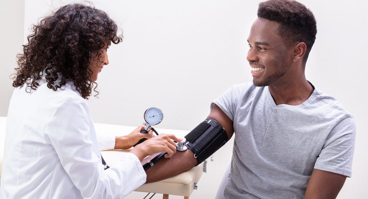 A young male patient undergoing in-house lab services as a doctor checks his pulse and blood pressure.
