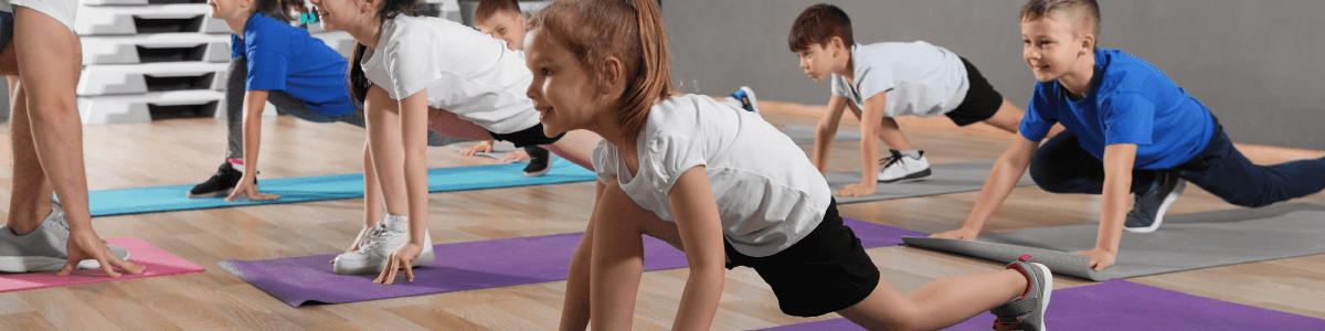 Children and trainer doing physical exercise in school gym.